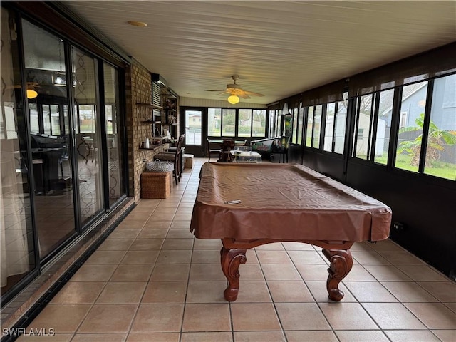 rec room with ceiling fan, tile patterned floors, a healthy amount of sunlight, and brick wall