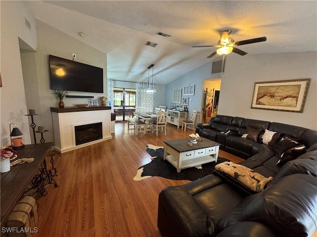 living room with ceiling fan, lofted ceiling, wood-type flooring, and a textured ceiling