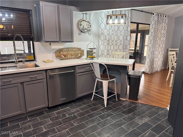 kitchen with a kitchen breakfast bar, gray cabinets, dishwasher, and sink