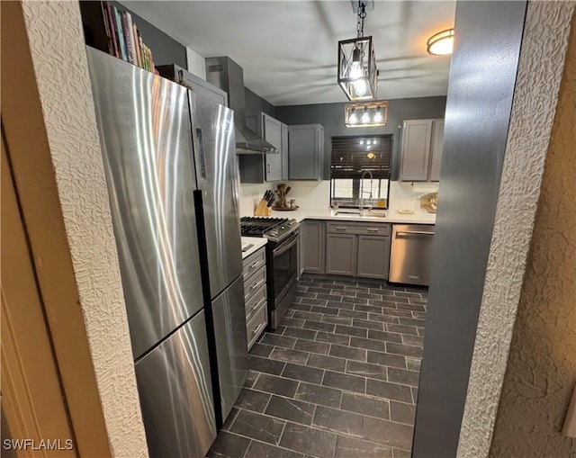 kitchen featuring wall chimney range hood, sink, appliances with stainless steel finishes, gray cabinetry, and hanging light fixtures