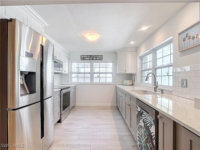 kitchen featuring appliances with stainless steel finishes, sink, white cabinets, a wealth of natural light, and light stone counters