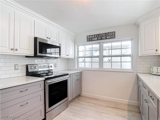 kitchen featuring light stone countertops, white cabinets, appliances with stainless steel finishes, light hardwood / wood-style floors, and backsplash