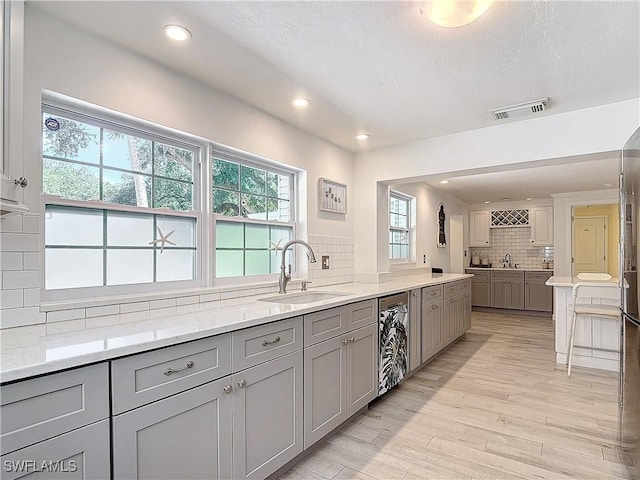 kitchen featuring sink, light stone countertops, gray cabinets, light hardwood / wood-style floors, and decorative backsplash