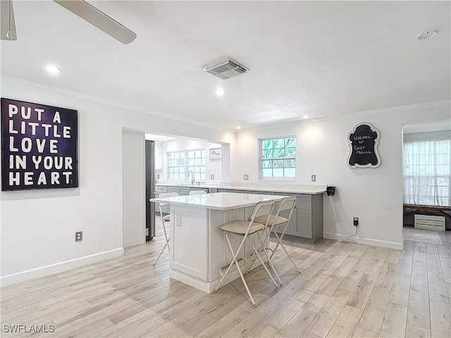 kitchen featuring a kitchen bar, light hardwood / wood-style floors, crown molding, gray cabinetry, and a kitchen island