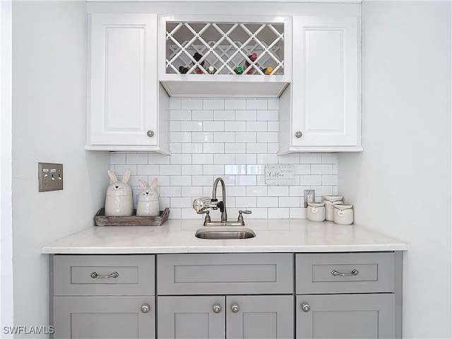 bar with light stone counters, sink, gray cabinetry, and tasteful backsplash