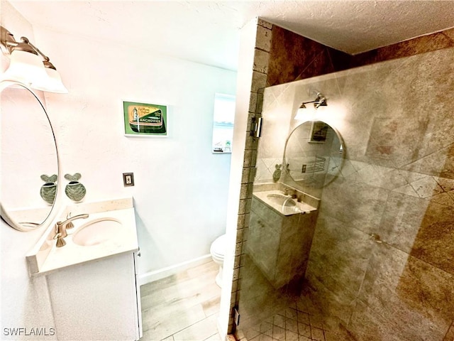 bathroom with toilet, a textured ceiling, wood-type flooring, a tile shower, and vanity