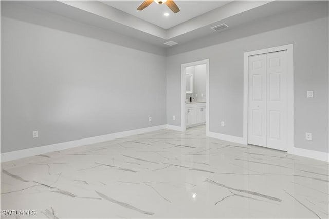 unfurnished bedroom featuring a raised ceiling, ensuite bathroom, ceiling fan, and a closet