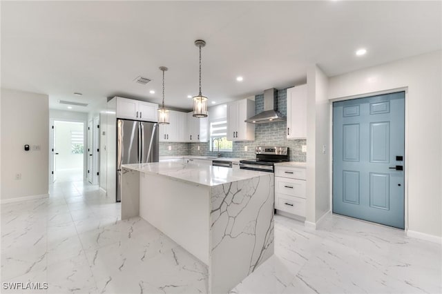 kitchen featuring a center island, white cabinets, pendant lighting, stainless steel appliances, and wall chimney exhaust hood