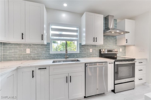 kitchen with appliances with stainless steel finishes, decorative backsplash, wall chimney range hood, white cabinets, and sink