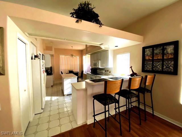 kitchen with white appliances, a kitchen breakfast bar, kitchen peninsula, and white cabinets