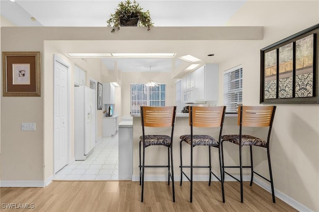 interior space with white appliances, a kitchen bar, a peninsula, white cabinetry, and light wood finished floors