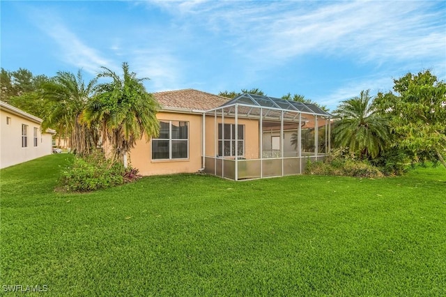 back of property with a yard, stucco siding, and glass enclosure