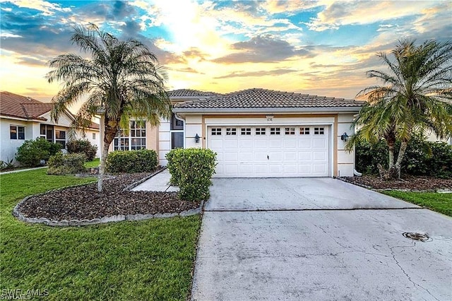 view of front of home with concrete driveway, stucco siding, a garage, a yard, and a tiled roof