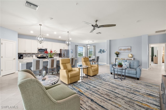 living room with ceiling fan with notable chandelier, visible vents, and light tile patterned flooring