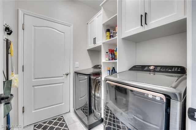 clothes washing area with cabinets, light tile patterned flooring, and washer and dryer