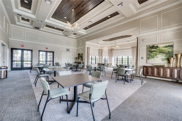 carpeted dining space with a chandelier, a high ceiling, ornamental molding, coffered ceiling, and french doors