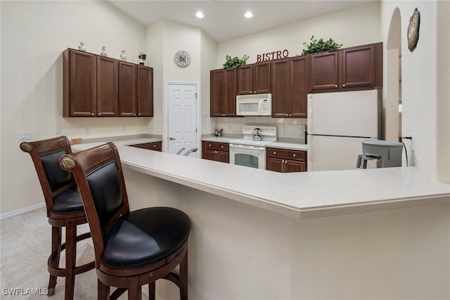 kitchen featuring kitchen peninsula, white appliances, a kitchen bar, and decorative backsplash