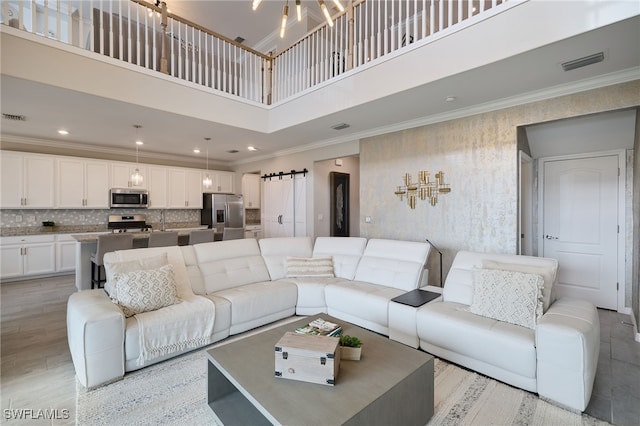 living room with crown molding, a towering ceiling, and a barn door