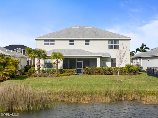 back of property with a lawn, a sunroom, and a water view