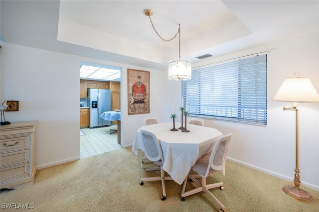 dining space with a raised ceiling and light colored carpet