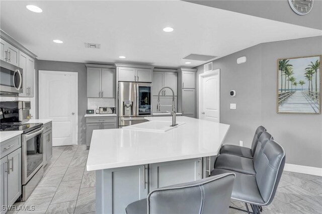 kitchen featuring sink, a center island with sink, gray cabinetry, and appliances with stainless steel finishes