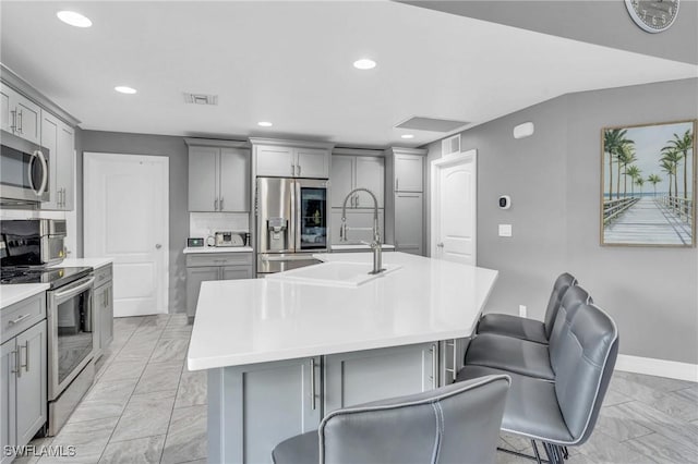 kitchen featuring gray cabinetry, sink, stainless steel appliances, and an island with sink