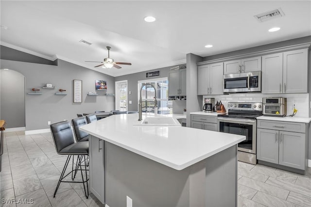 kitchen with vaulted ceiling, a kitchen island with sink, gray cabinetry, stainless steel appliances, and a breakfast bar area