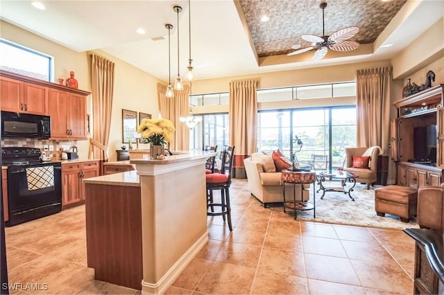 kitchen with a kitchen bar, a tray ceiling, pendant lighting, light stone countertops, and black appliances