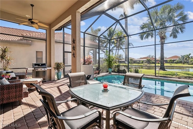 view of patio with grilling area, a water view, ceiling fan, and glass enclosure