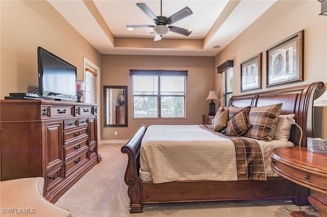 bedroom with light colored carpet, ceiling fan, and a tray ceiling