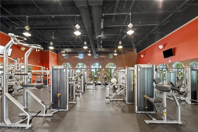 workout area featuring track lighting, brick wall, and a high ceiling