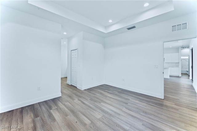 empty room with a raised ceiling and light hardwood / wood-style floors