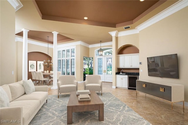 living room with an inviting chandelier, ornate columns, wine cooler, and a raised ceiling