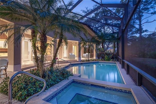 pool at dusk featuring an in ground hot tub and glass enclosure