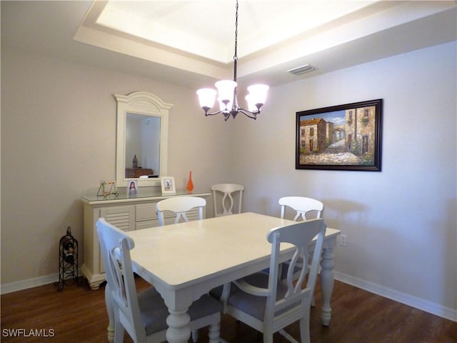 dining room featuring dark wood-type flooring, a tray ceiling, and an inviting chandelier