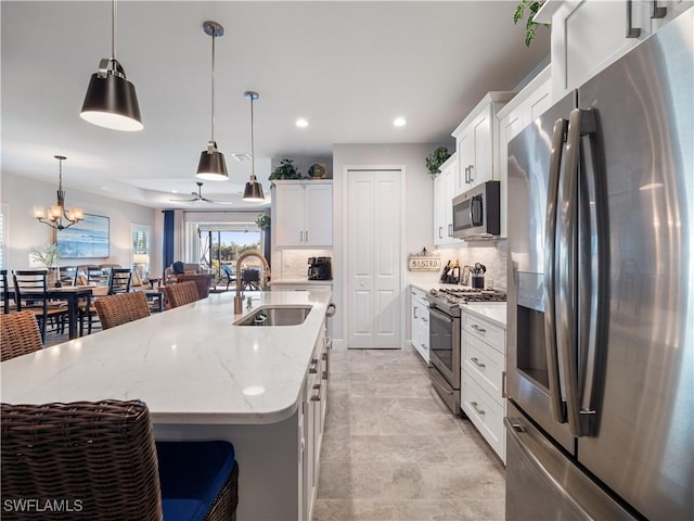 kitchen featuring appliances with stainless steel finishes, white cabinetry, hanging light fixtures, sink, and a center island with sink