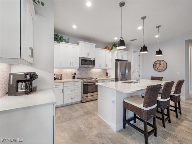 kitchen with an island with sink, white cabinetry, hanging light fixtures, and appliances with stainless steel finishes