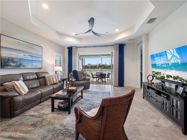 living room featuring ceiling fan and a raised ceiling