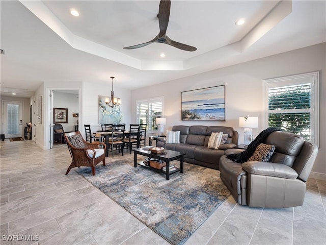 living room featuring ceiling fan with notable chandelier and a raised ceiling