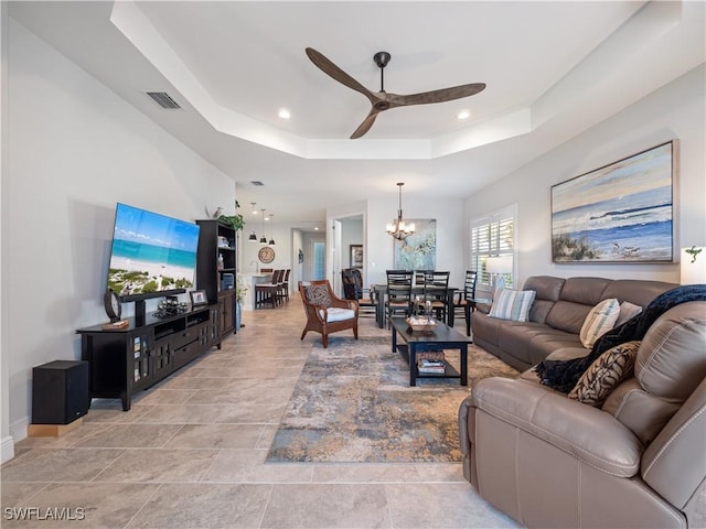 living room with ceiling fan with notable chandelier and a raised ceiling