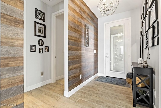 foyer entrance with wooden walls, a chandelier, and light wood-type flooring