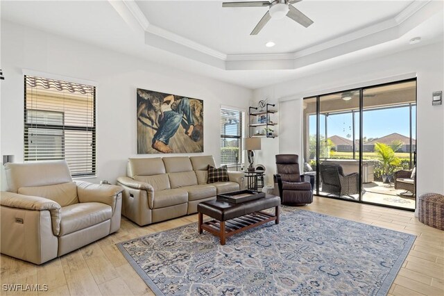 living room with crown molding, light hardwood / wood-style floors, a raised ceiling, and ceiling fan