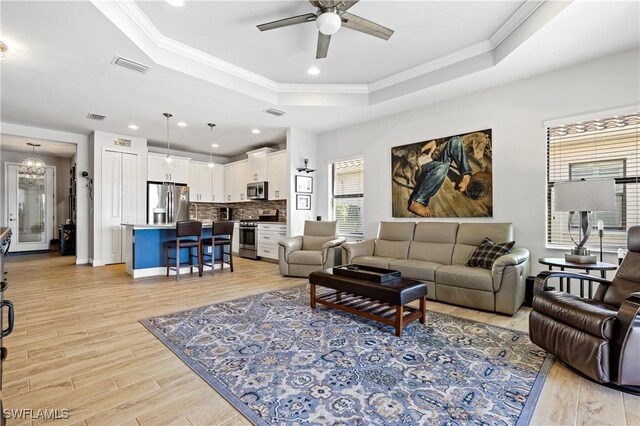 living room featuring a tray ceiling, ceiling fan with notable chandelier, ornamental molding, and light wood-type flooring