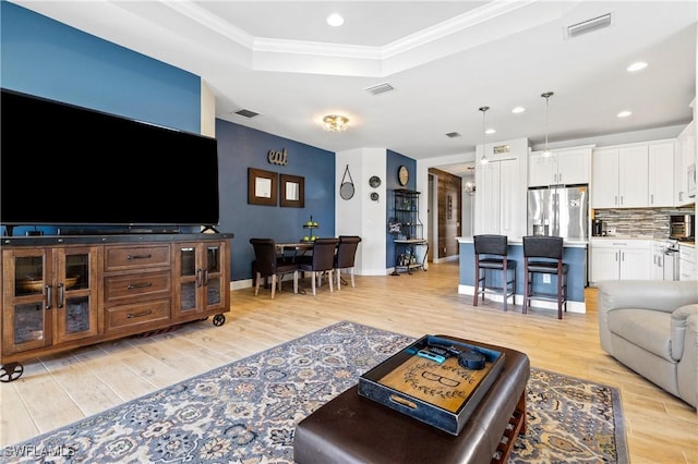 living room featuring crown molding, a tray ceiling, and light hardwood / wood-style floors