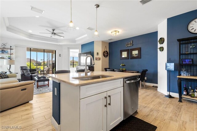 kitchen featuring white cabinetry, a center island with sink, stainless steel dishwasher, a tray ceiling, and pendant lighting