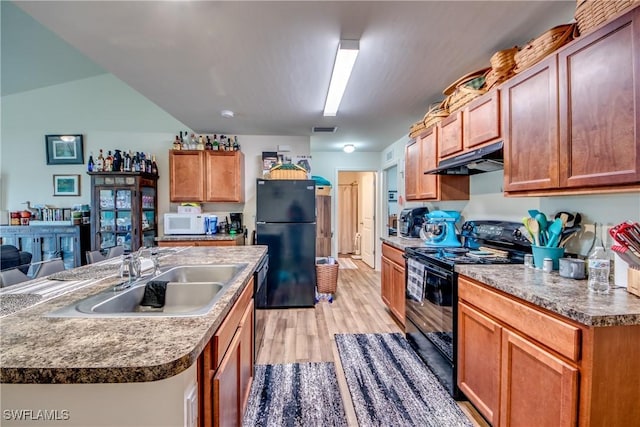 kitchen with vaulted ceiling, sink, black appliances, a center island with sink, and light wood-type flooring