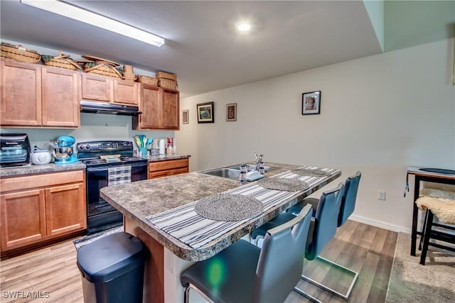 kitchen with an island with sink, sink, a kitchen breakfast bar, black electric range, and light wood-type flooring