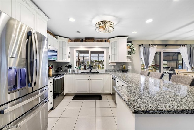 kitchen with appliances with stainless steel finishes, white cabinetry, light tile patterned floors, kitchen peninsula, and dark stone counters