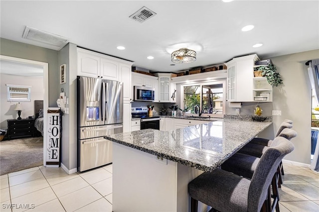 kitchen with white cabinetry, stainless steel appliances, dark stone countertops, a kitchen breakfast bar, and kitchen peninsula