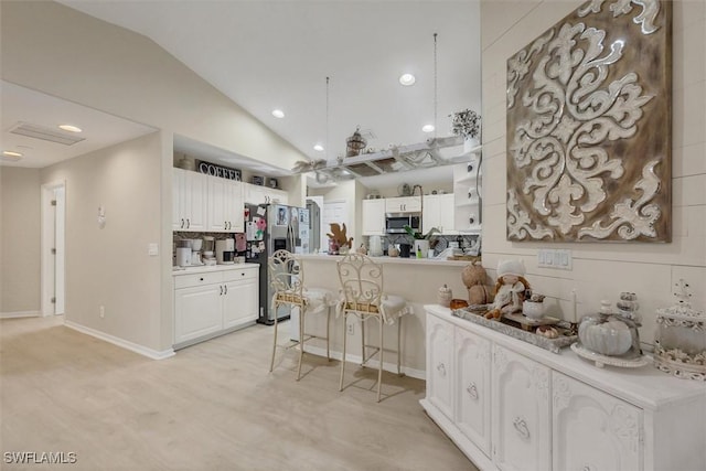 kitchen featuring appliances with stainless steel finishes, white cabinets, kitchen peninsula, a breakfast bar area, and lofted ceiling